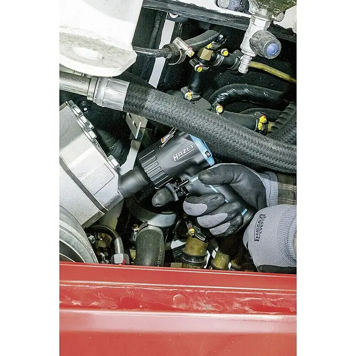Hazet Druckluft-Schlagschrauber 9012M - Antriebsgröße: ½″, Betriebsdruck: 6,3 bar - Nahaufnahme des Hazet-Schlagschraubers 9021SPC im Einsatz, gehalten von behandschuhten Händen inmitten eines komplexen Motorraums.