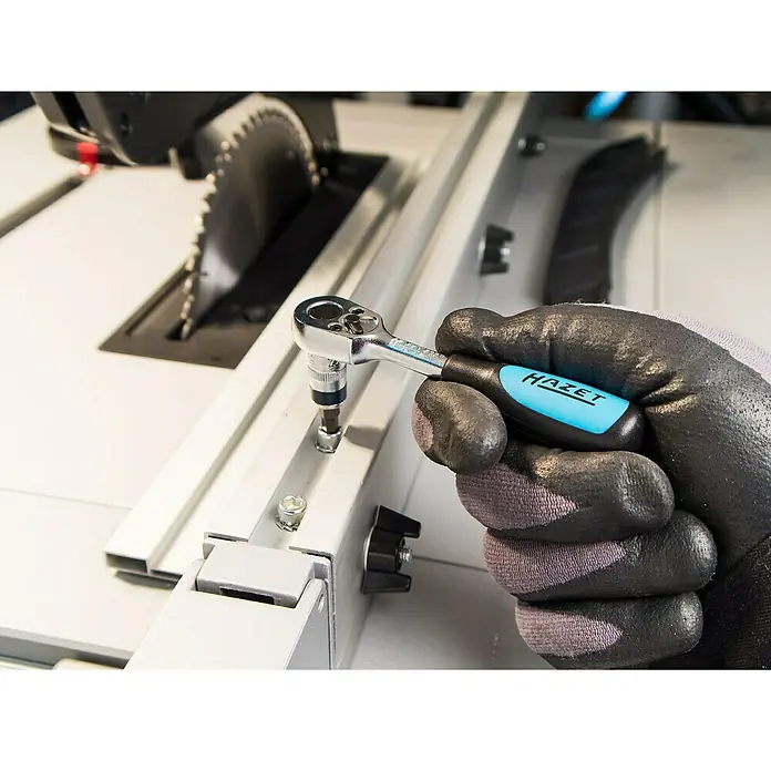 Hazet Steckschlüsseleinsatz-Set 853-1 - ¼″, 36 -tlg. - Eine Hand mit Handschuh hält einen HAZET Mini-Ratschenschraubendreher mit Bit, der an einer Schraube an einer Tischsäge befestigt wird.