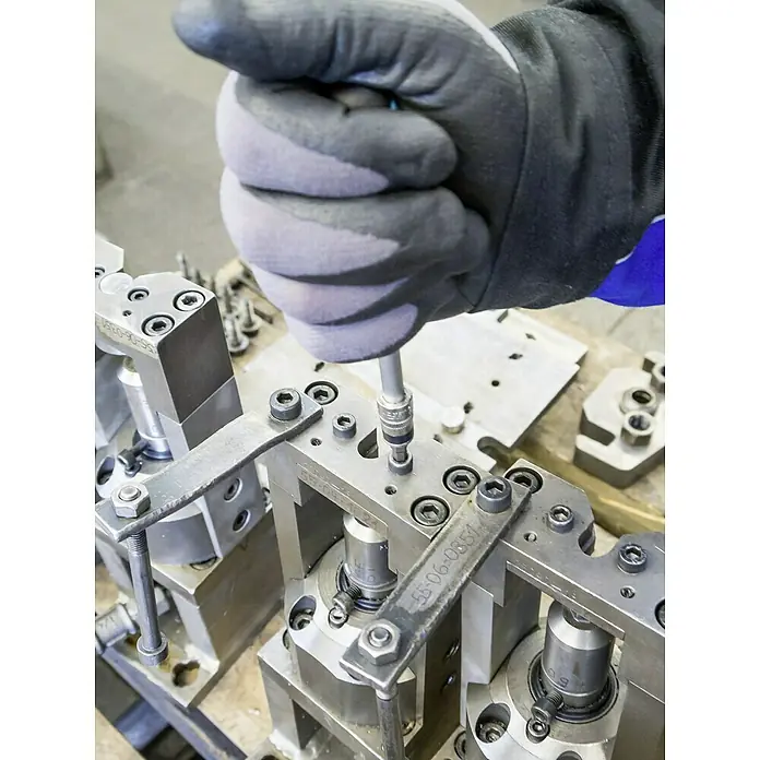 Hazet Steckschlüsseleinsatz-Set 853-1 - ¼″, 36 -tlg. - Ein Bediener, der einen Schraubenschlüssel benutzt, um ein Bauteil auf einer silberfarbenen Metallvorrichtung zu befestigen, wobei die Vorrichtung im Fokus steht.