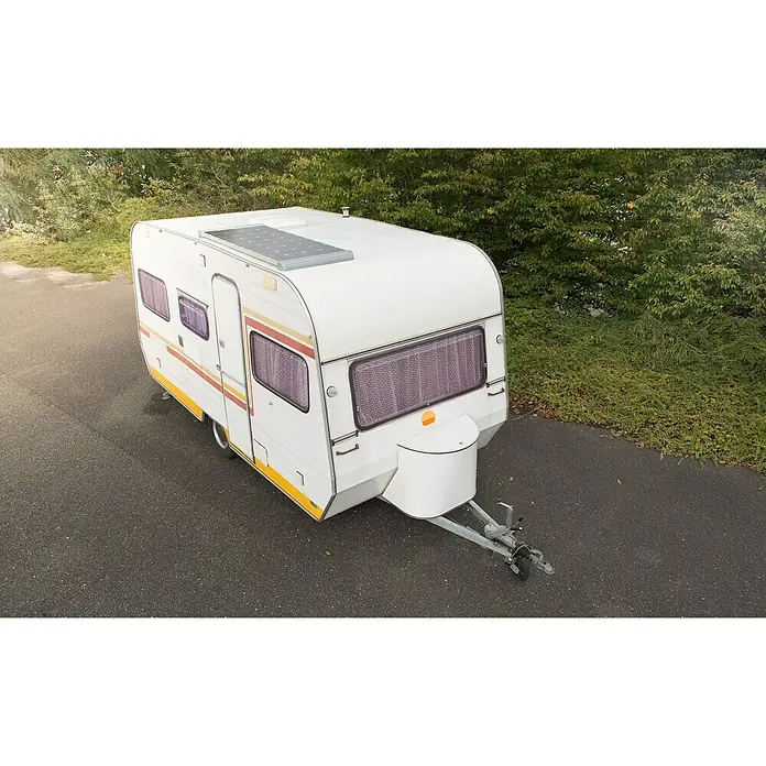 Sunset Solarmodul-Set Caravan - Nennleistung: 140 W, Für den Caravan- und Campingbereich - Ein weißer Wohnwagen mit gelben und roten Streifen, der auf einer asphaltierten Straße mit Bäumen im Hintergrund steht. Auf dem Dach befindet sich ein Solarpanel.