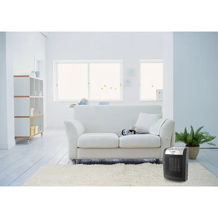 Voltomat HEATING Heizlüfter - 900 kW - 1.800 W, Schwarz, 12 x 17 x 22 cm - Hier ist ein Bild eines Keramikraumheizers in einem hellen Wohnzimmer, der auf einem Teppich vor einem Sofa steht.