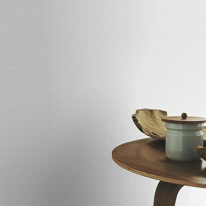 Rasch Vliestapete Feel Good Glasfaser-Optik - Weiß, Uni, 10,05 x 0,53 m, Wabenstruktur - Das Bild zeigt einen Tisch mit einer Keramikdose mit Holzdeckel und einer Holzschale, arrangiert vor einem strukturierten, weißen Hintergrund.