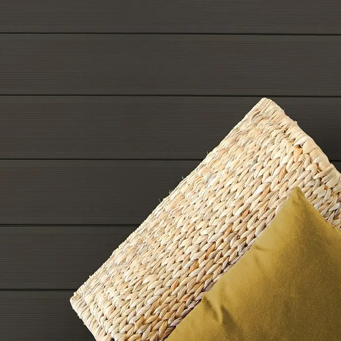 Kovalex WPC-Terrassendiele Massiv strukturo nach Maß - 300 x 14,5 x 2 cm, Grau-Braun - Nahaufnahme eines Korbs mit beigem Kissen vor einer grauen Holzvertäfelung, die Textur und natürliche Materialien hervorhebt.