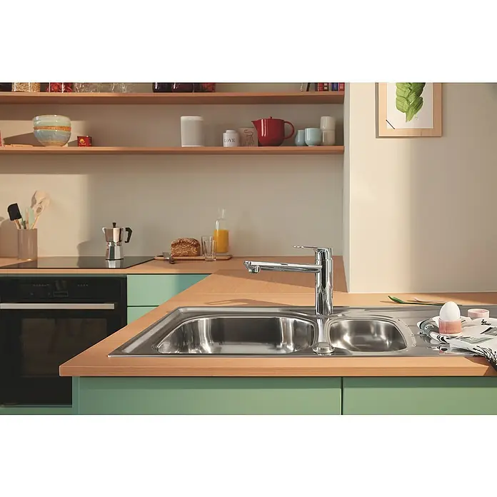 Grohe QuickFix Start Loop Grifo de cocina - Profundidad del grifo: 222 mm, Cromo, Brillo intenso - Fregadero de acero inoxidable con grifo moderno en una cocina elegante con armarios verdes claros y estantes de madera.