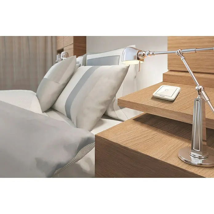 Bosch Smart Home Universalschalter Flex - Reichweite Funk: 200 m - Intelligentes Bosch-Gerät auf einem Nachttisch neben einem Bett, mit Fokus auf das schlanke Design und die Integration in ein modernes Schlafzimmer.