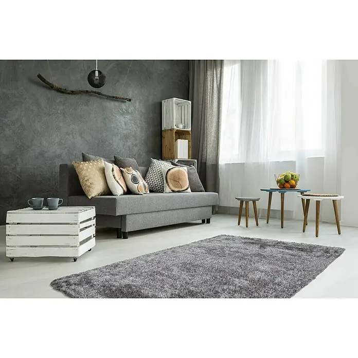 Kayoom Hochflorteppich DiamondGrau/Weiß, 170 x 120 cm, 100 % Polyester - Ein Wohnzimmer mit einem grauen Teppich, einem Sofa und Beistelltischen. Der Teppich ist flauschig und bedeckt einen großen Teil des Bodens.