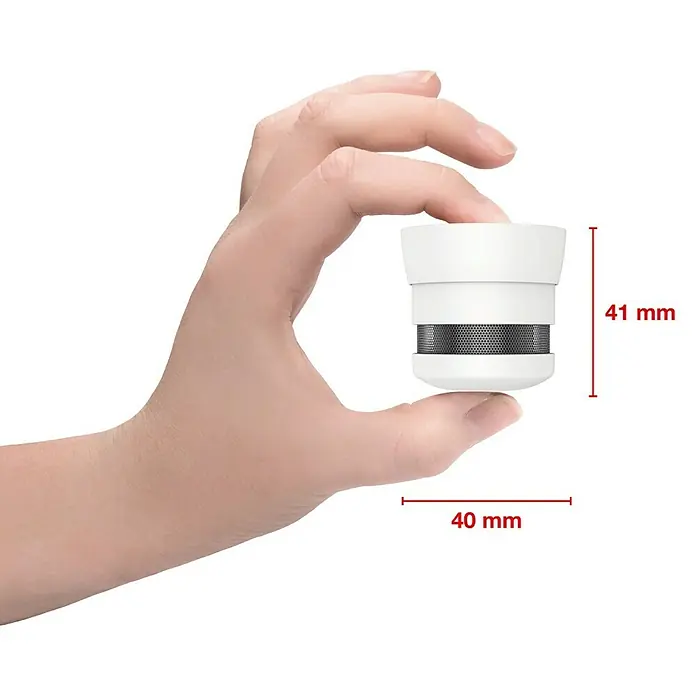 Gloria Rauchwarnmelder RC-10 - Ø x H: 40 x 41 mm, Batterielaufzeit: 10 Jahre - Hand hält einen kleinen, weißen Rauchmelder. Der Rauchmelder ist kompakt und zylindrisch, mit einem schwarzen Gitter in der Mitte.