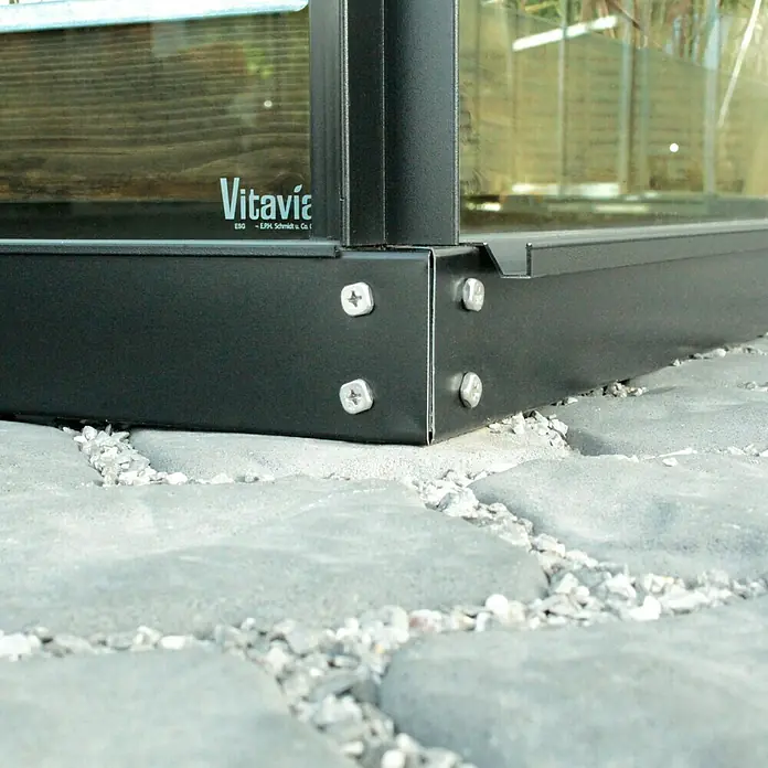 Vitavia Gewächshaus-Fundament - 441 x 254 x 6 cm, Passend für: Vitavia Gewächshaus Dione 11500/Mars 11500/Merkur 11500/Uranus 11500, Schwarz - Detailaufnahme einer schwarzen Vitavia Gewächshauskonstruktion, befestigt mit Schrauben auf einem Steinboden, die Marke Vitavia ist erkennbar.