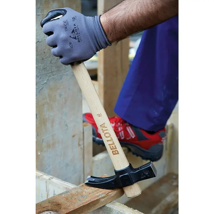 Bellota Martillo de albañil 8030CI - Largo: 43 mm, 600 g, Acero - Primer plano de un martillo BELLOTA con mango de madera, sujetado por una mano con un guante de trabajo, sacando un clavo de una tabla de madera.