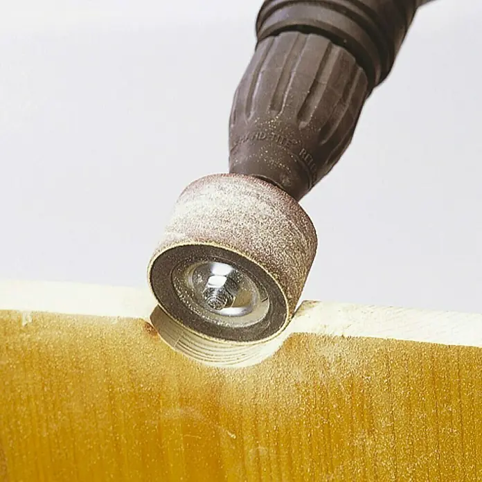 Wolfcraft Disco pulidor - Ø x Al: 45 x 30 mm - Primer plano de un tambor de lijado acoplado a un taladro, suavizando el borde de una superficie de madera, ideal para trabajos de madera detallados.