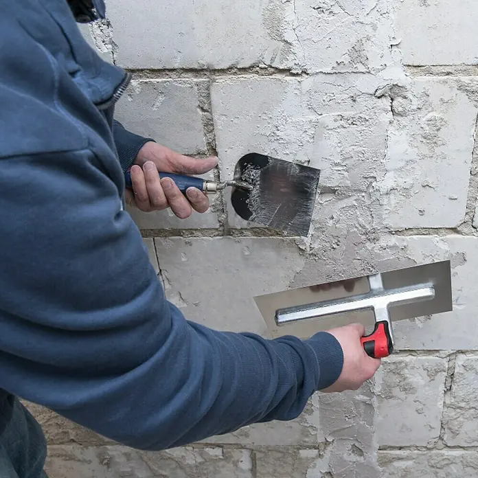 Connex Llana de alisado COX781242 - 130 x 280 mm - Artesano alisando una pared de ladrillos con dos espátulas para crear una superficie plana. Herramientas para trabajos de construcción en acción.