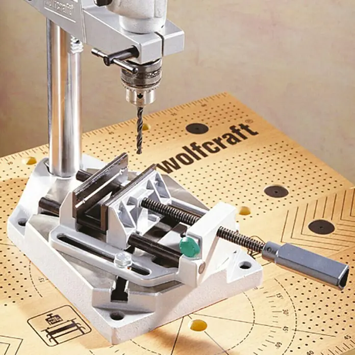 Wolfcraft Mordaza de sujeción - Anchura de sujeción: 100 mm - Primer plano de un soporte de taladro Wolfcraft con tornillo de banco sobre un banco de trabajo con patrón de cuadrícula.