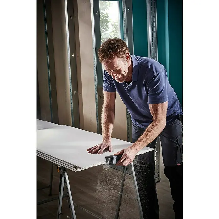 Wolfcraft Cepillo Surform manual 4013000 - Plástico - Hombre lija paneles de yeso con una herramienta de lijado en un banco de trabajo en un taller.