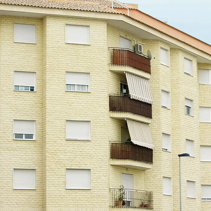 Revestimiento de piedra Teide - 14 x 28 cm, Crema - Fachada de un edificio de apartamentos amarillo con persianas enrollables y balcones, mostrando arquitectura moderna.