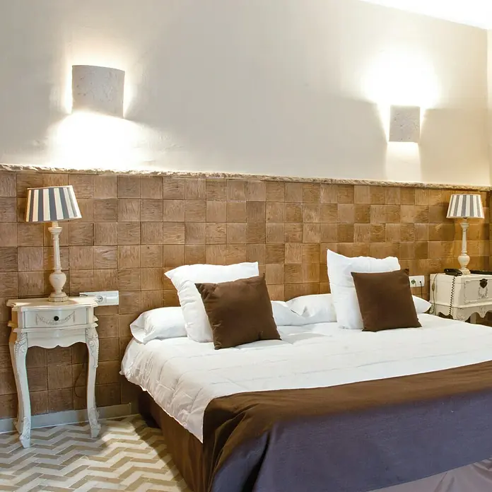 Revestimiento de piedra Teka - Cantidad total: 4 pzs. - Una acogedora habitación de hotel con una cama grande, mesitas de noche con lámparas y una pared de madera.