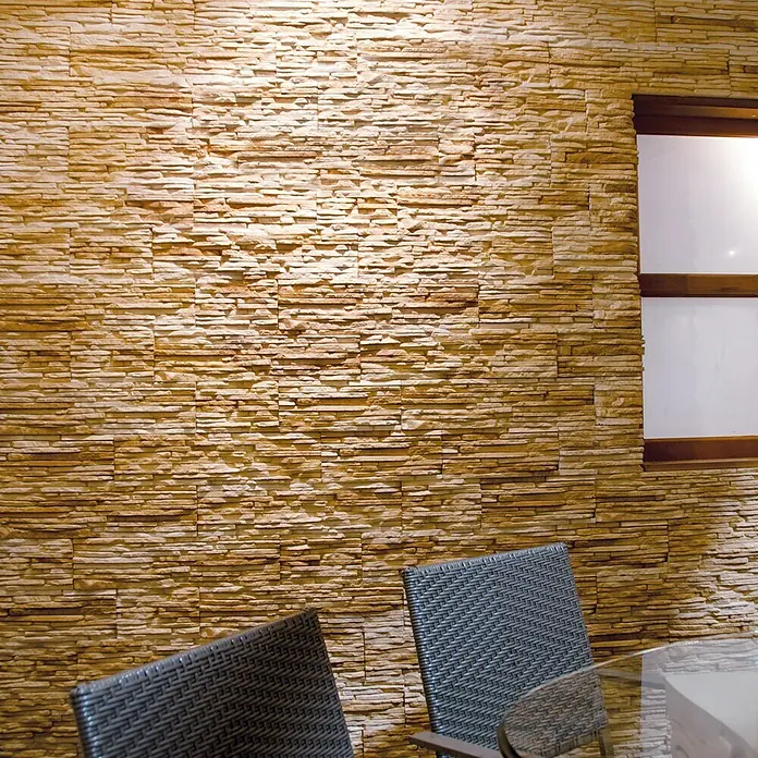 Revestimiento de piedra Galicia - Bronce, Cantidad total: 4 pzs. - Pared de acento texturizada con dos sillas de ratán y mesa de vidrio. La pared consta de piedras horizontales en tonos beige y marrón.