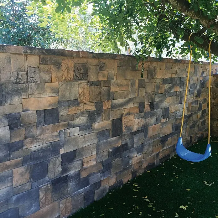 Revestimiento de piedra Montblanc Otoño - Cantidad total: 4 pzs. - Primer plano de un columpio azul para niños colgado de un árbol contra una pared de piedra, creando un espacio de jardín lúdico y acogedor.