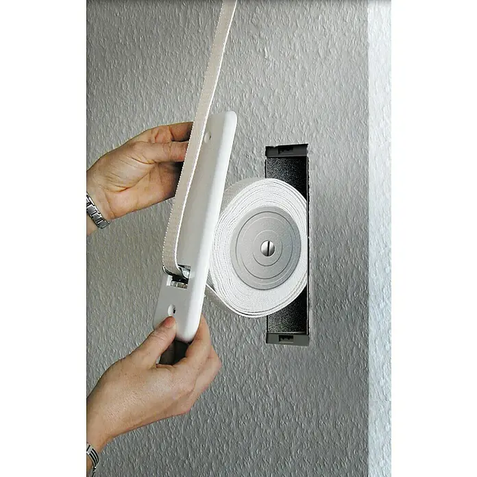 Schellenberg Polea 50401 - Distancia entre orificios: 185 mm, Anchura de la correa: 23 mm, Zincado - Control de persiana: Primer plano de una persona instalando una persiana enrollable con cinta en una pared.
