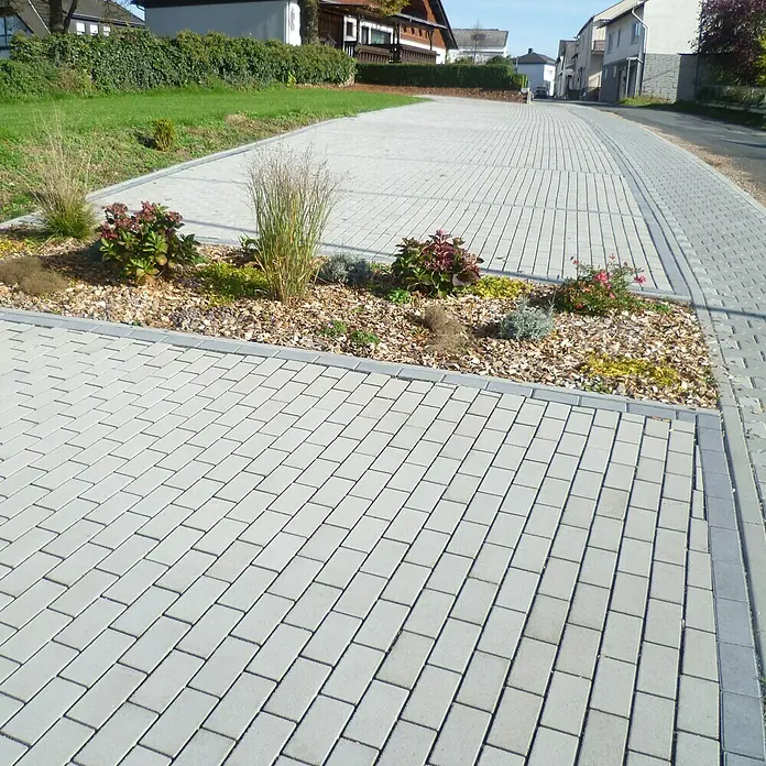 EHL Pflasterstein Drän - Grau, 20 x 10 x 8 cm, Rechteckig - Blick auf eine Pflasterfläche mit rechteckigen Pflastersteinen und einem bepflanzten Beet in der Mitte. Die Steine sind hellgrau und wirken modern.