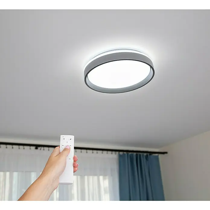 Garza Plafón LED redondo Panda - 60 W, Negro, Blanco frío - Una mano sujeta un mando a distancia para controlar una moderna lámpara de techo LED con borde gris y forma redonda.