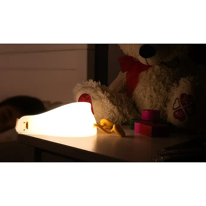 Garza Lámpara de sobremesa LED Pato Kiko - L x An x Al: 1.210 x 103 x 62 mm, 5 W, Intensidad regulable - Una linda luz nocturna con forma de pingüino que emite un brillo suave y relajante junto a un oso de peluche en una mesita de noche.