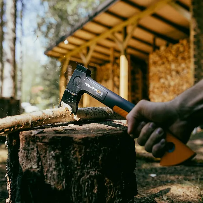 Fiskars X-series Universalaxt X14 - Länge: 35,5 cm - Nahaufnahme einer Axt der Marke Fiskars beim Holzspalten, ideal für Gartenarbeit und Outdoor-Aktivitäten.