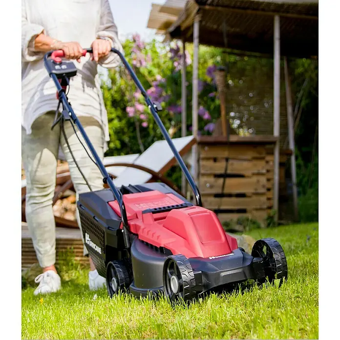 Hurricane Elektro-Rasenmäher HERM-I-1232 - 1.200 W, Schnittbreite: 32 cm - Eine Frau benutzt einen roten und schwarzen Hurricane Rasenmäher im Garten, um das Gras zu mähen.