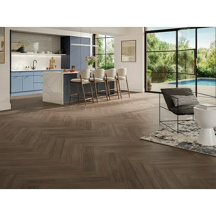 Parador Designbodenmuster Modular ONE Eiche Artemis kaffeebraun - 200 x 140 x 9 mm, Fischgrät - Elegantes Interieur mit dunklem Holzboden im Fischgrätmuster, das dem Raum Wärme und Stil verleiht. Moderne Küche und bequeme Sitzecke im Hintergrund.