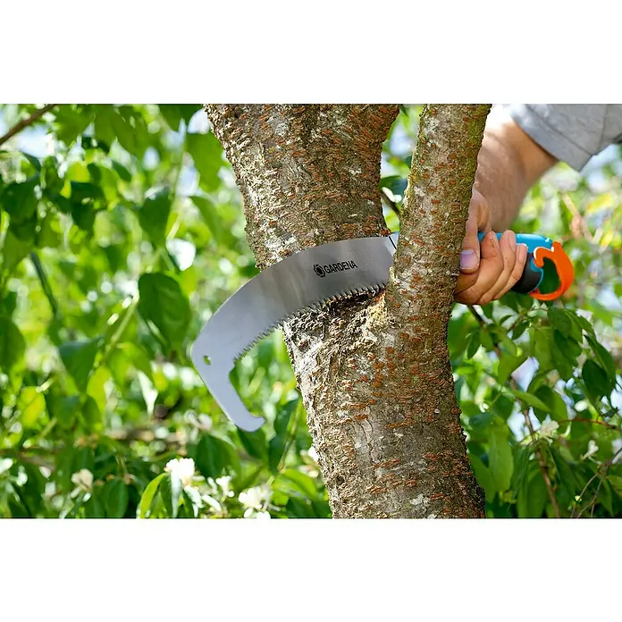 Gardena Combisystem Sierra de podar manual 300PP - Largo: 556 mm, Plástico, Plateado, Turquesa - Primer plano de una sierra de podar Gardena cortando la rama de un árbol, rodeada de follaje verde.