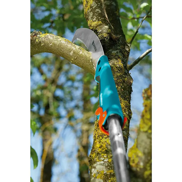 Gardena Combisystem Sierra de podar manual 300PP - Largo: 556 mm, Plástico, Plateado, Turquesa - Sierra de ramas en acción: una sierra de ramas Gardena cortando una rama en un árbol, rodeada de follaje verde y cielo azul.