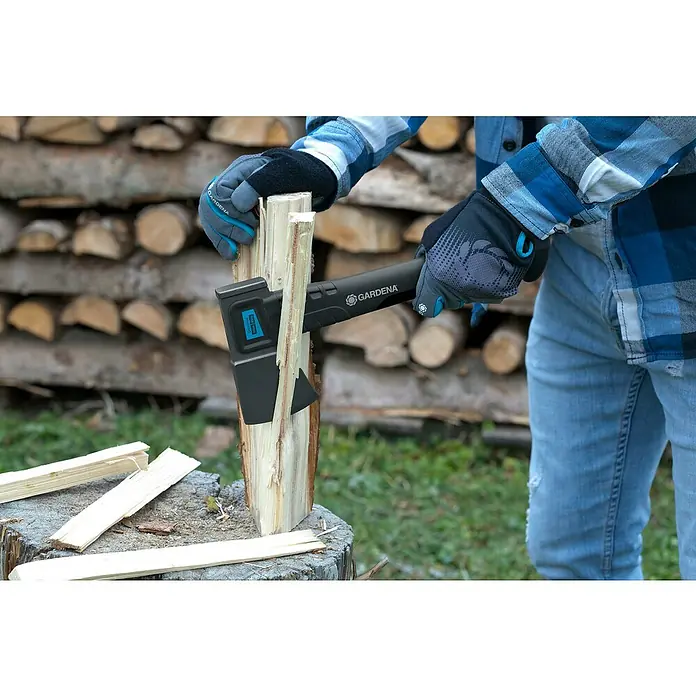 Gardena Spaltaxt 1600 S - Länge: 628 mm - Nahaufnahme einer Person, die mit einer Gardena Axt Holz spaltet, mit einem Stapel Holz im Hintergrund.