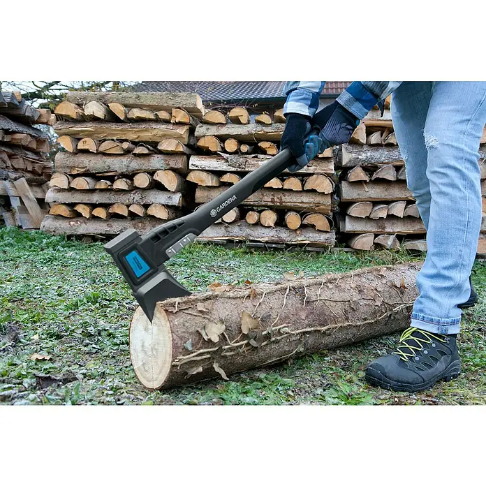 Gardena Spaltaxt 1600 S - Länge: 628 mm - Eine Axt der Marke Gardena steckt in einem Holzscheit, im Hintergrund gestapeltes Brennholz. Die Axt ist ein nützliches Werkzeug für die Holzbearbeitung.