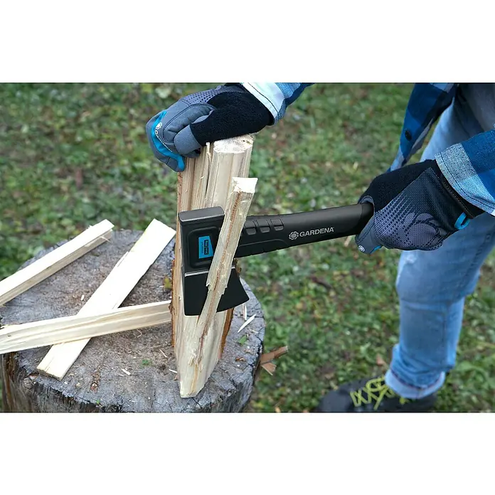 Gardena Universalbeil 900 B - Länge: 34 cm - Nahaufnahme einer Axt der Marke Gardena, die in einem Holzstamm steckt, mit abgeschnittenen Holzstücken auf einem Baumstumpf im Freien.