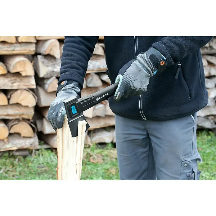Gardena Universalbeil 900 B - Länge: 34 cm - Eine Person spaltet Holz mit einer Gardena Axt. Das Beil ist schwarz und blau, während die Person graue Handschuhe und graue Hosen trägt.