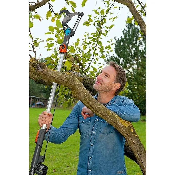 Gardena Combisystem Cortarramas de jardín - Grosor de rama máx.: 35 mm, Mango tipo D con resistente cable de tracción, sistema de guardado de cable (sin enredos) y fijación de cable - Un hombre está usando una podadora de árboles telescópica Gardena para cortar ramas en un árbol mientras está en un jardín.