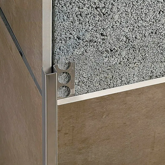 Perfil cuadrado multiusos Brillo - Acero inoxidable, Plateado, 12 mm - Primer plano de un perfil de borde de baldosa plateado entre baldosas y una pared de hormigón, destacando el borde limpio.