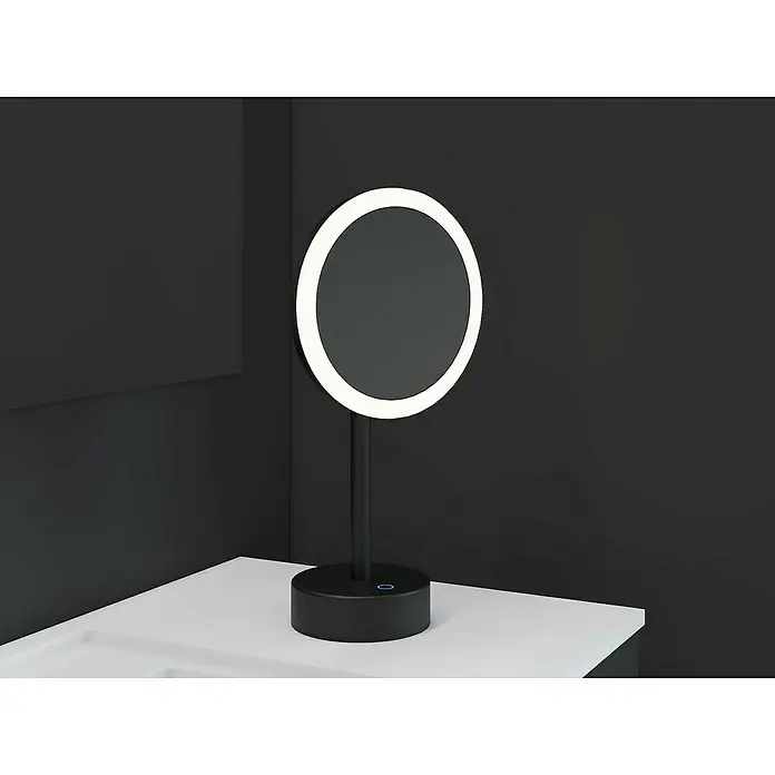 Cosmic Espejo cosmético de encimera Essentials - Negro - Un espejo de maquillaje redondo iluminado negro se encuentra sobre un tocador blanco contra una pared oscura.