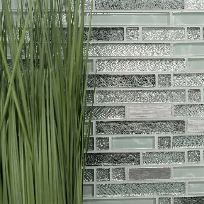 Mosaikfliese Verbund Crystal Mix XCM MV698 - 29,8 x 30,4 cm, Grau/Silber, Glänzend - Ein Blick auf eine dekorative Wandfliese mit Glas- und Metallic-Akzenten, teilweise verdeckt durch grüne Dekorationen.