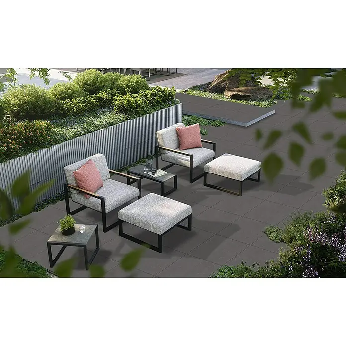Terrassenfliese Basalt 2.0 - 59,7 x 59,7 x 2 cm, Basaltgrau, Matt - Elegante Outdoor-Lounge mit grauen Sesseln, Hockern und Beistelltischen auf dunklen Fliesen, umgeben von üppigem Grün. Perfekt für entspannte Stunden im Freien.