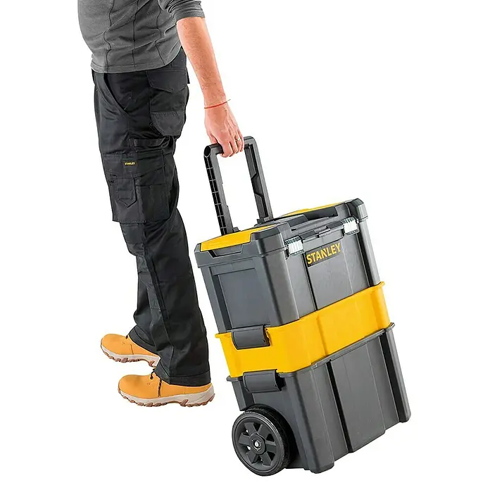 Stanley Rollende Profi-Box - Ohne Werkzeug, L x B x H: 47,5 x 28,5 x 62,3 cm - Eine Person zieht einen grauen und gelben Stanley Werkzeugkoffer mit Rädern und ausziehbarem Griff.