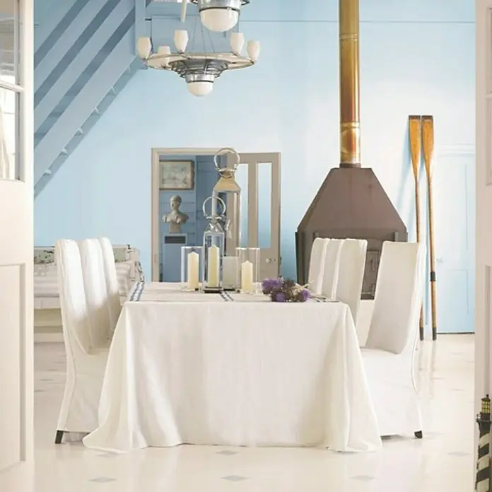 Bruguer Esmalte blanco para puertas - Blanco roto, 2,5 l, Satinado - Elegante comedor con paredes azules, un mantel blanco y sillas a juego. Una chimenea acogedora añade calidez y ambiente.