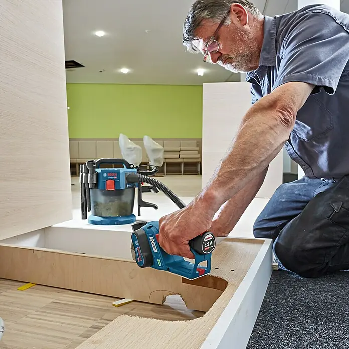 Bosch Professional Akku-Handhobel GHO 12V-20 - 12 V, Ohne Akku, 14.500 U/min - Handwerker bei der Arbeit mit einem blauen Bosch Multifunktionswerkzeug, das mit einem 12V-Akku betrieben wird.