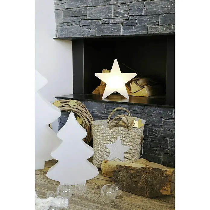 8 Seasons Design Shining LED-Stern Star - Außen, 10 cm, Neutralweiß - Festliche Szene mit leuchtendem Stern, dekorativen Weihnachtsbäumen und einem rustikalen Korb vor einem Steinkamin.