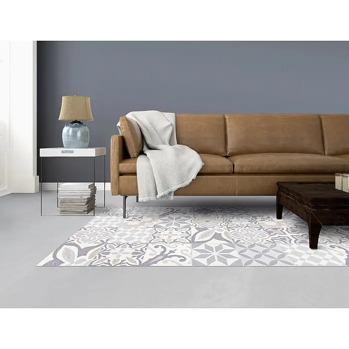 Alfombra de vinilo Croma BCN vintage - Pastel azul, 180 x 120 cm - Imagen de una sala de estar con un sofá de cuero marrón y una alfombra estampada. Una lámpara y libros están sobre una mesa pequeña.