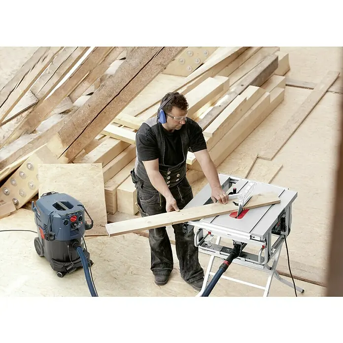 Bosch Professional Elektro-Nass- & Trockensauger GAS 35 M AFC - 1.200 W, Behältervolumen: 35 l, Mit Beutel - Der Handwerker benutzt eine Bosch Tischkreissäge, um ein Holzbrett zu bearbeiten, und trägt dabei Schutzkleidung.