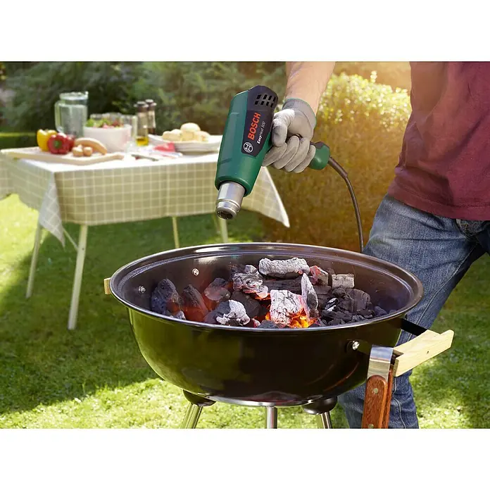 Bosch Heißluftgebläse EasyHeat 500 - 1.600 W, Temperaturbereich: 300 °C - 500 °C - Eine Nahaufnahme eines Bosch EasyHeat 500 Heißluftgebläses, das zum Anzünden von Holzkohle in einem Grill im Freien verwendet wird.