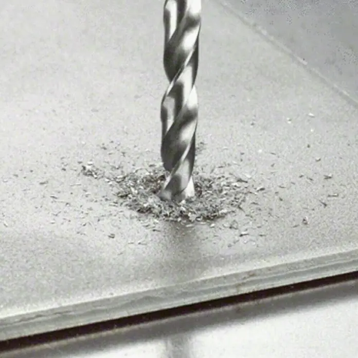 Bosch Broca para metal HSS-G - Diámetro de la broca: 4,5 mm, Longitud de trabajo: 47 mm - Primer plano de una broca helicoidal que perfora un agujero en una placa de metal, rodeada de virutas metálicas.
