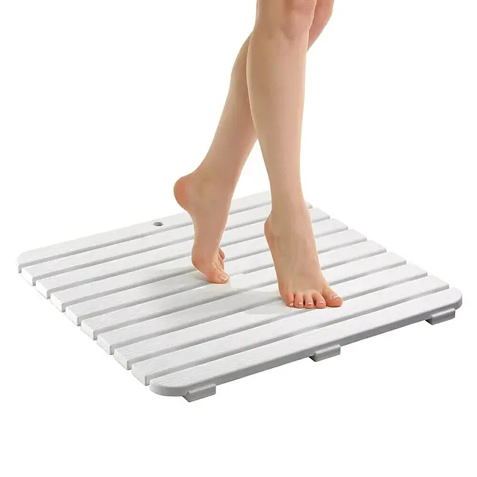 Tatay Tarima de baño - L x An: 55 x 55 cm, Blanco, Polipropileno - Primer plano de una alfombra de baño de madera blanca con pies femeninos encima. La alfombra de baño proporciona una superficie antideslizante para baños.
