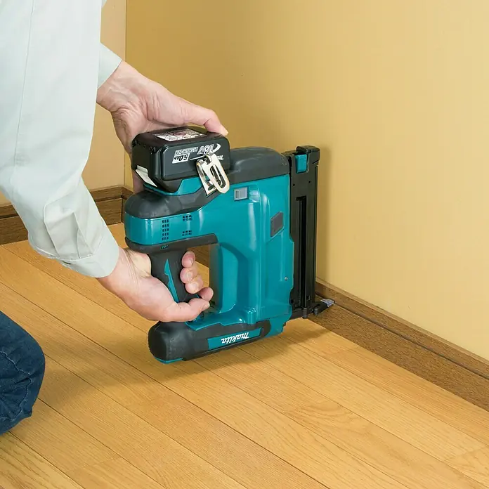 Makita LXT 18V Akku-Nagler DBN500RTJ - 18 V, 2 Akkus, 5 Ah, Länge Nagel: 15 mm - 50 mm - Akku-betriebener Makita-Nagler wird von einer Person an einer Wand in der Nähe einer Fußleiste verwendet.