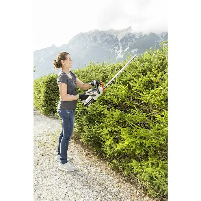 AL-KO 36V Akku-Heckenschere HT 4055 - 36 V, Li-Ionen, Ohne Akku, Schnittlänge: 55 cm - Eine Frau schneidet mit einer AL-KO Akku-Heckenschere eine Hecke. Die Heckenschere ist weiß und hat ein rotes Detail.